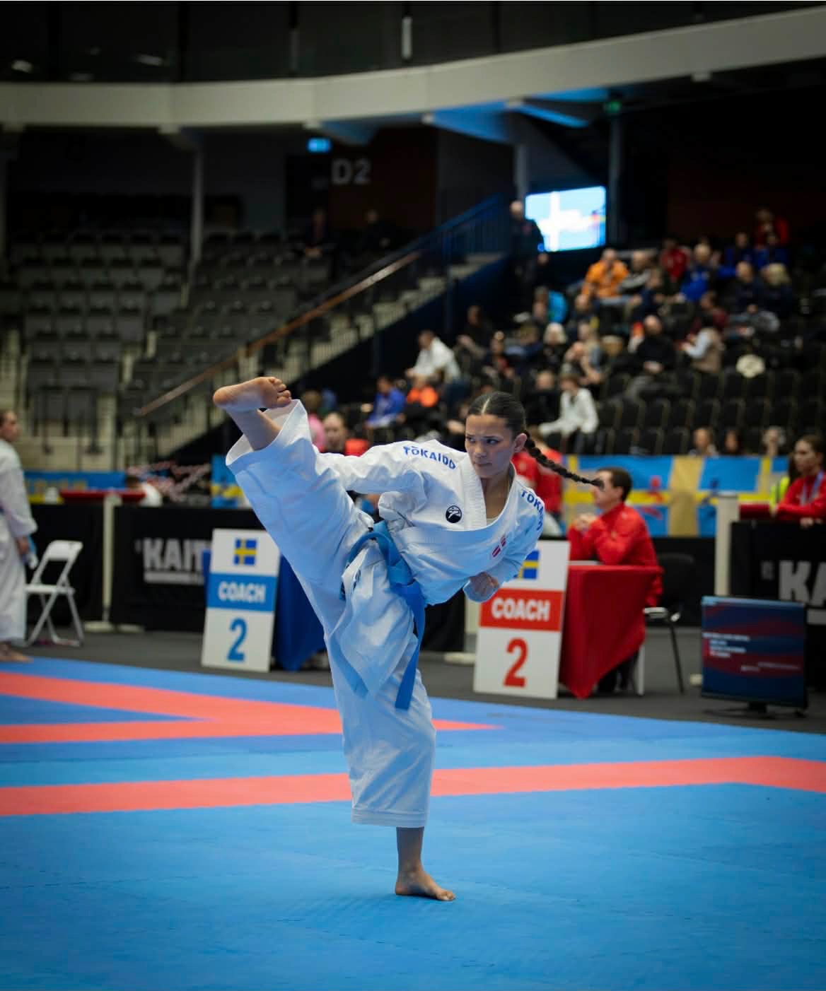 Freja Chung Jepsen performing a high kick during kata on the competition mat in a large arena