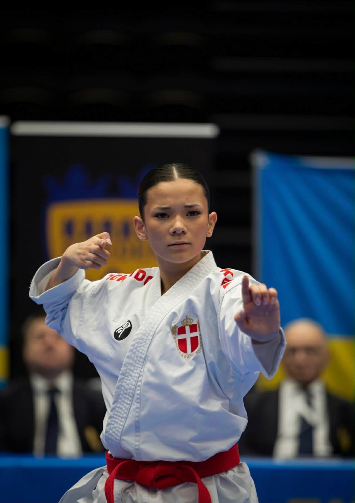 Close-up of Freja Chung Jepsen in a Denmark karate gi with a red belt, mid-kata in front of the judges